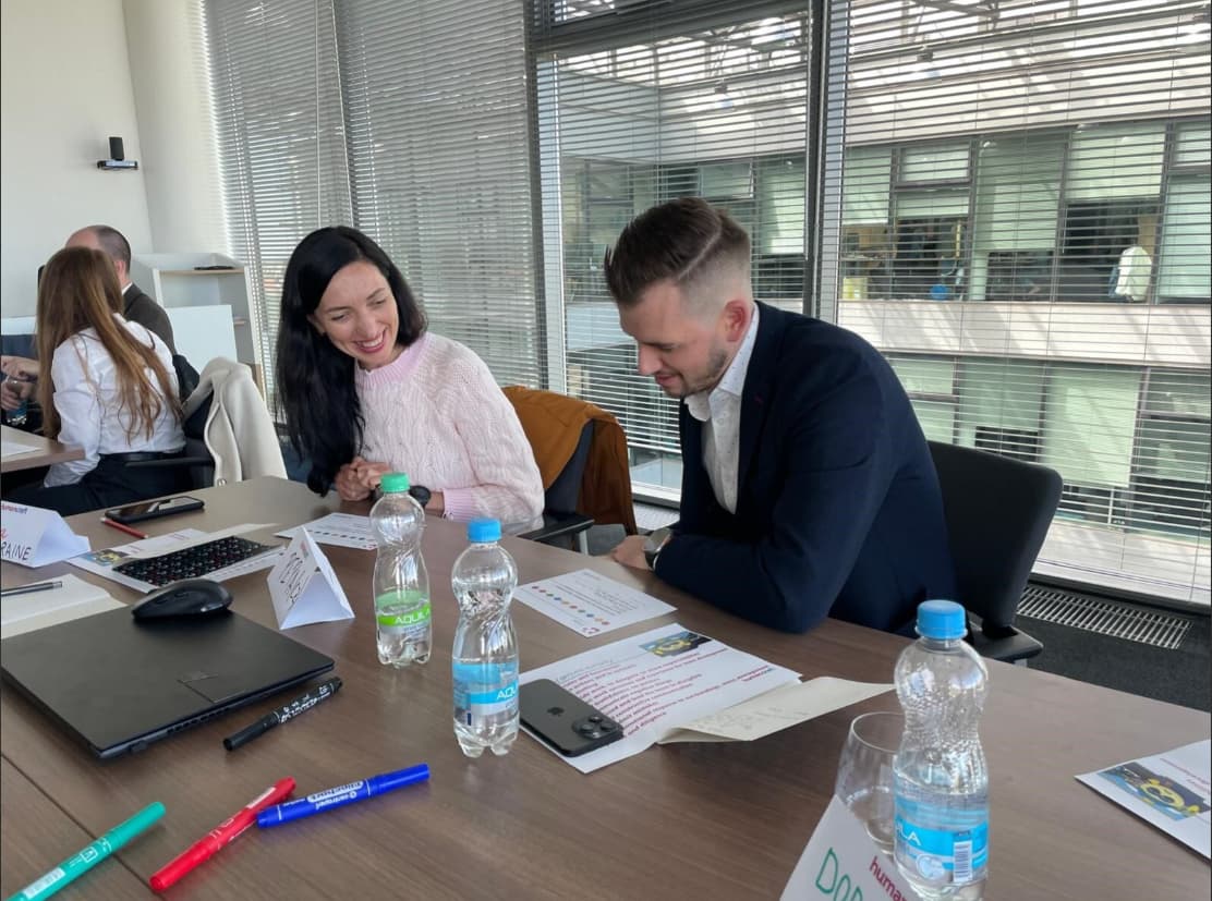Teamdiskussion und Durchsicht von Dokumenten im modernen Büro Zwei Kollegen sehen sich gedruckte Dokumente an und besprechen die Ergebnisse an einem Tisch mit Wasser, Markern und einem Laptop in einem hellen Büro mit großen Fenstern