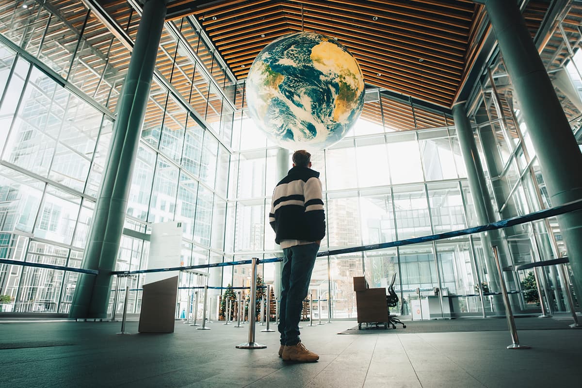 Person standing in a modern interior beneath a suspended globe, symbolizing data collection, analysis, and structuring for ESG and sustainable business developmen
